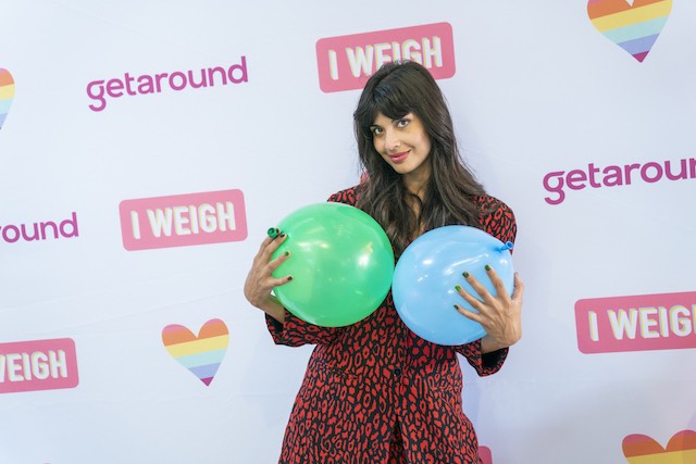 Jameela Jamil, a woman of color with long brown hair holding two air balloons in front of her chest.