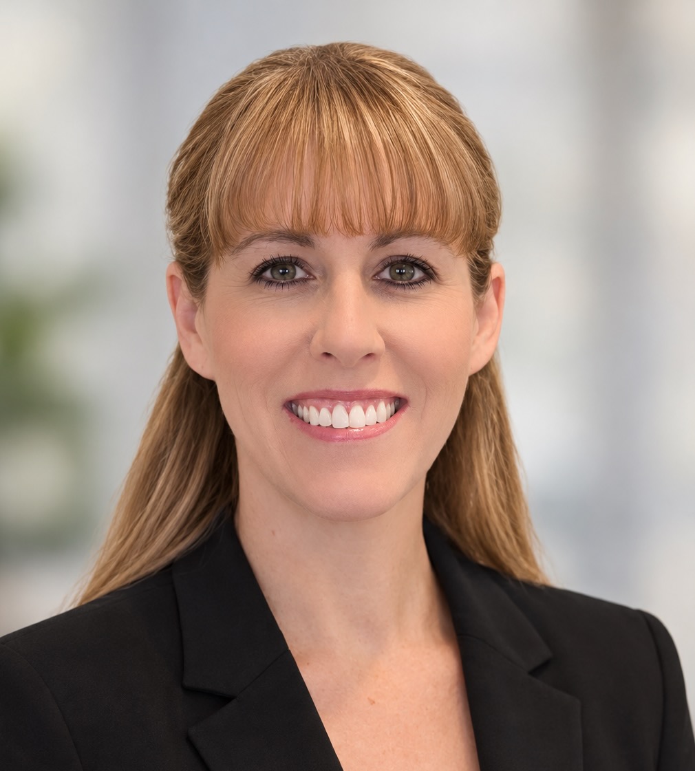 Professional headshot of Melissa McNulty, PhD with light brown hair and bangs, smiling at the camera. She is wearing a black blazer over a black top against a softly blurred, light neutral background.