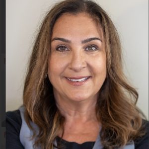 Professional headshot of Donna with shoulder-length brown hair, wearing a dark top and light gray vest, against a neutral background.