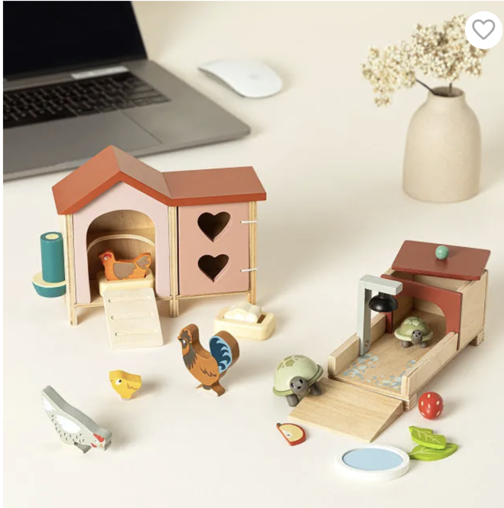 A small wooden chicken coop and reptile house sit on a desk near a laptop. There are small wooden chickens, turtles, and other pet accessories like water dishes. 