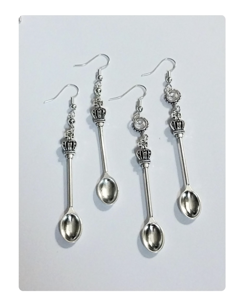 Two pairs of silver earrings in the shape of spoons with a decorative bead between the fancy handle of the spoon and the earring hardware. 