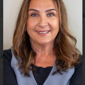 Professional headshot of Donna with shoulder-length brown hair, wearing a dark top and light gray vest, against a neutral background.