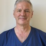 Head-and-shoulders portrait of Professor Mark S. Whiteley wearing navy blue medical scrubs embroidered with 
