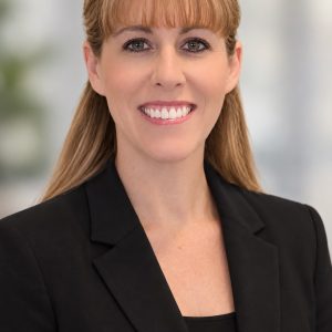 Professional headshot of Melissa McNulty, PhD with light brown hair and bangs, smiling at the camera. She is wearing a black blazer over a black top against a softly blurred, light neutral background.